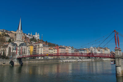 Bridge over river by buildings against blue sky