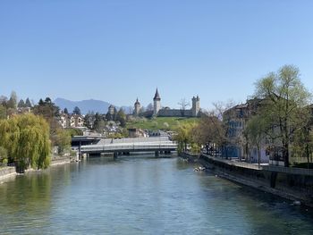 Bridge over river by buildings against clear sky