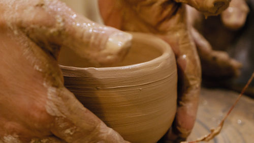 Cropped hands of potter making pot on pottery wheel