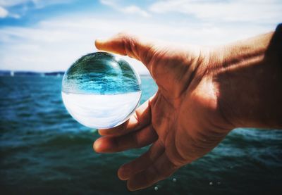 Cropped hand holding crystal ball against sea