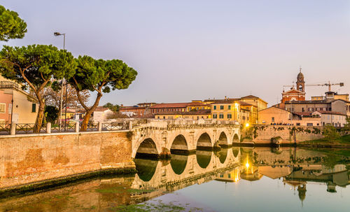 Bridge over river by buildings in city against clear sky