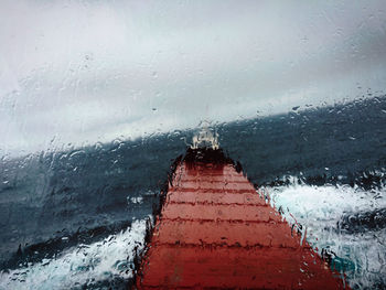 Close-up of wet window against sky during winter