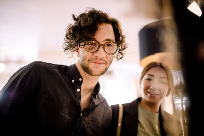 Smiling man trying fashionable eyeglasses with friend at store
