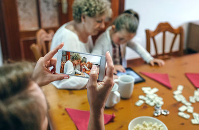 Woman photographing daughter with grandmother from mobile phone at home