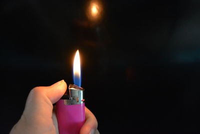 Close-up of hand holding lit candle against black background