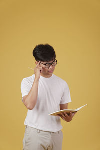 Midsection of man holding umbrella while standing against yellow wall