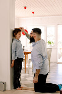 Father measuring daughter's height against wall at home