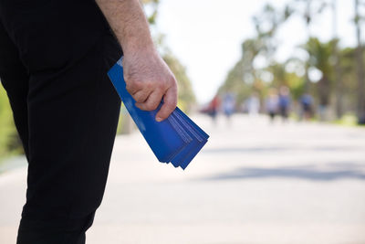 Midsection of man holding envelop on road against sky