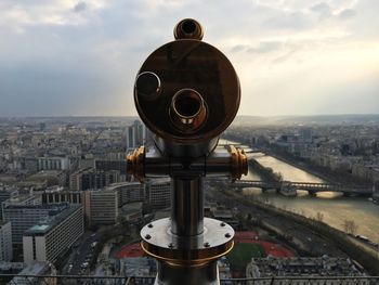 Coin-operated binoculars in front of seine river and buildings in city at sunset