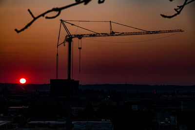 Silhouette cranes against sky at sunset