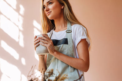 Young woman looking away while standing against wall