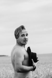 Side view of shirtless man standing at beach against sky