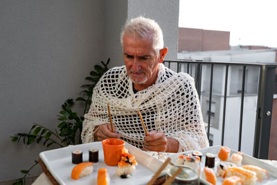 Attractive middle-aged man have fun while eating sitting at a table laid chinese  food on a terrace