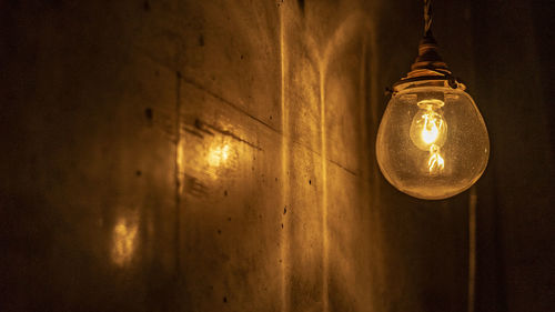 Low angle view of illuminated light bulb hanging on ceiling