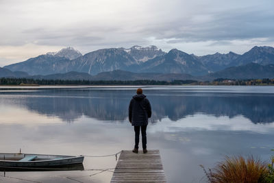 Rear view of man standing on lake against mountains