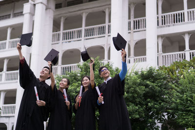 Students in university gowns holding mortarboards while standing against building