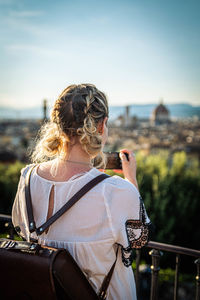 Rear view of woman photographing railing against sky