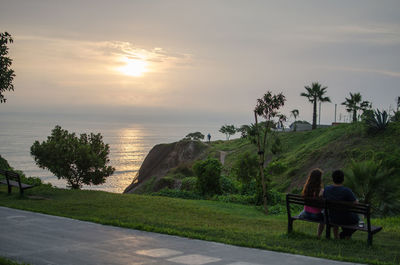 Rear view of people sitting on bench at sunset