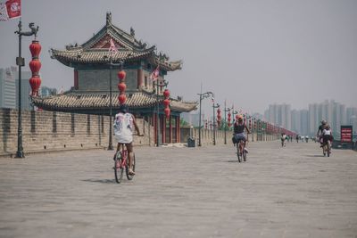 People riding bicycle by drum tower in xi an against sky