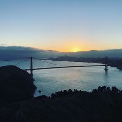 Suspension bridge over sea against sky during sunset