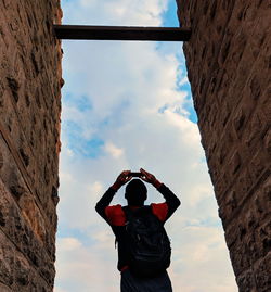 Rear view of man photographing by stone wall against cloudy sky