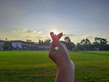 Human hand on field against sky