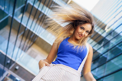 Low angle portrait of smiling young woman standing against building in city