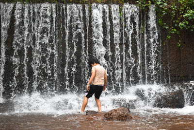 Rear view of boy standing in waterfall