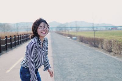 Portrait of smiling young woman standing against sky