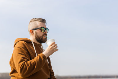 Man drinking smoothie against sky