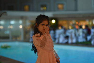 Portrait of angry girl pointing while standing at poolside during night