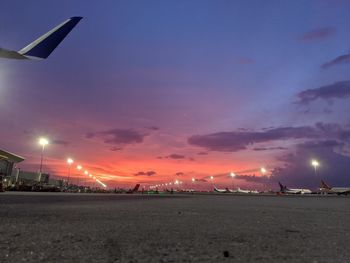 Illuminated street by city against sky during sunset