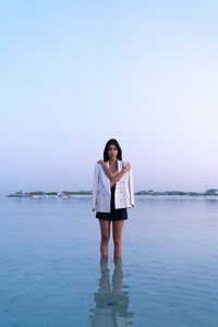 Portrait of a beautiful middle eastern woman walking in the water wearing a jacket hugging herself