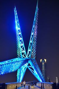 Low angle view of illuminated bridge against blue sky at night