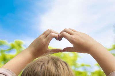 Close-up of child making heart shape against sky