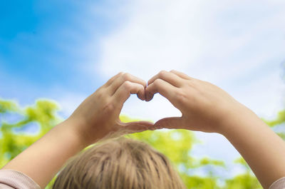 Midsection of woman making heart shape against sky