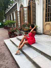 Side view of woman sitting on potted plant against building