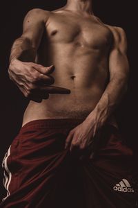 Midsection of shirtless man standing against black background