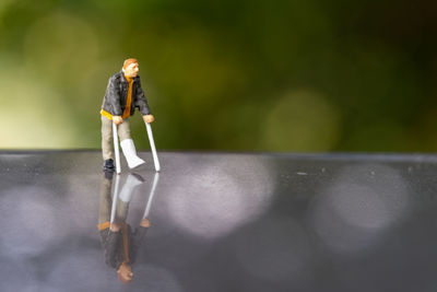 Miniature people , full length view of a man with broken leg is using crutch for walking