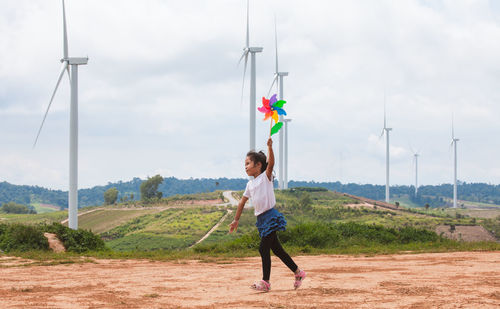 Full length of girl playing with pinwheel toy on land with windmills in background