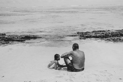 Rear view of shirtless man sitting on beach