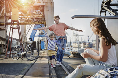 Germany, hamburg, father and daughter balancing on rail at the harbor