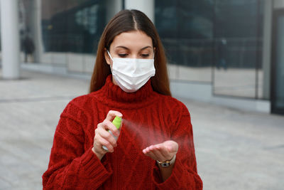 Young woman wearing mask using hand sanitizer
