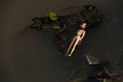 Plastic female doll abandoned in river, old toy, plastic object polluting waters in river.
