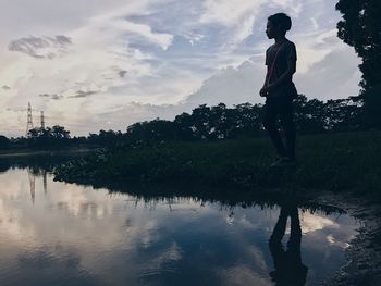 Reflection of man in lake against sky during sunset