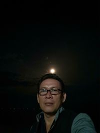 Portrait of young man wearing eyeglasses against sky at night