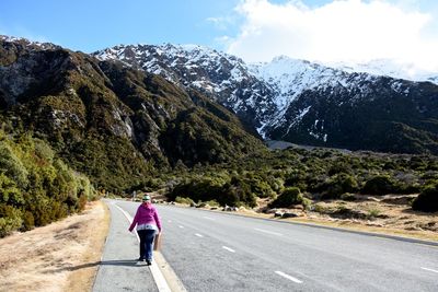 Rear view of woman walking on road leading toward mountain