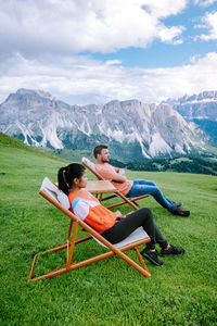 People sitting on grass by mountains against sky