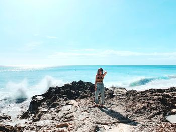 Woman standing on rock formation at beach against sky