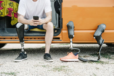 Young man with leg prosthesis sitting in camper van using cell phone